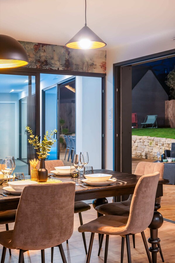 A dining area with a table set for four, chairs, a vase with plants, and a view of the outdoors.