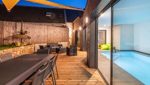 An outdoor patio with a pool, wooden deck, and seating area. - La Longère du Verger, Maison de 200m2 Avec Piscine Intèrieure, et Plage à Pied (Trégunc)