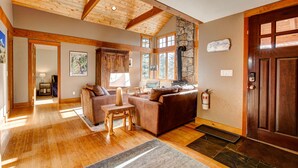 A spacious living room with wooden flooring, a stone fireplace, and a large wooden door. - Evergreen View - A Modern Mountain Retreat (Estes Park)