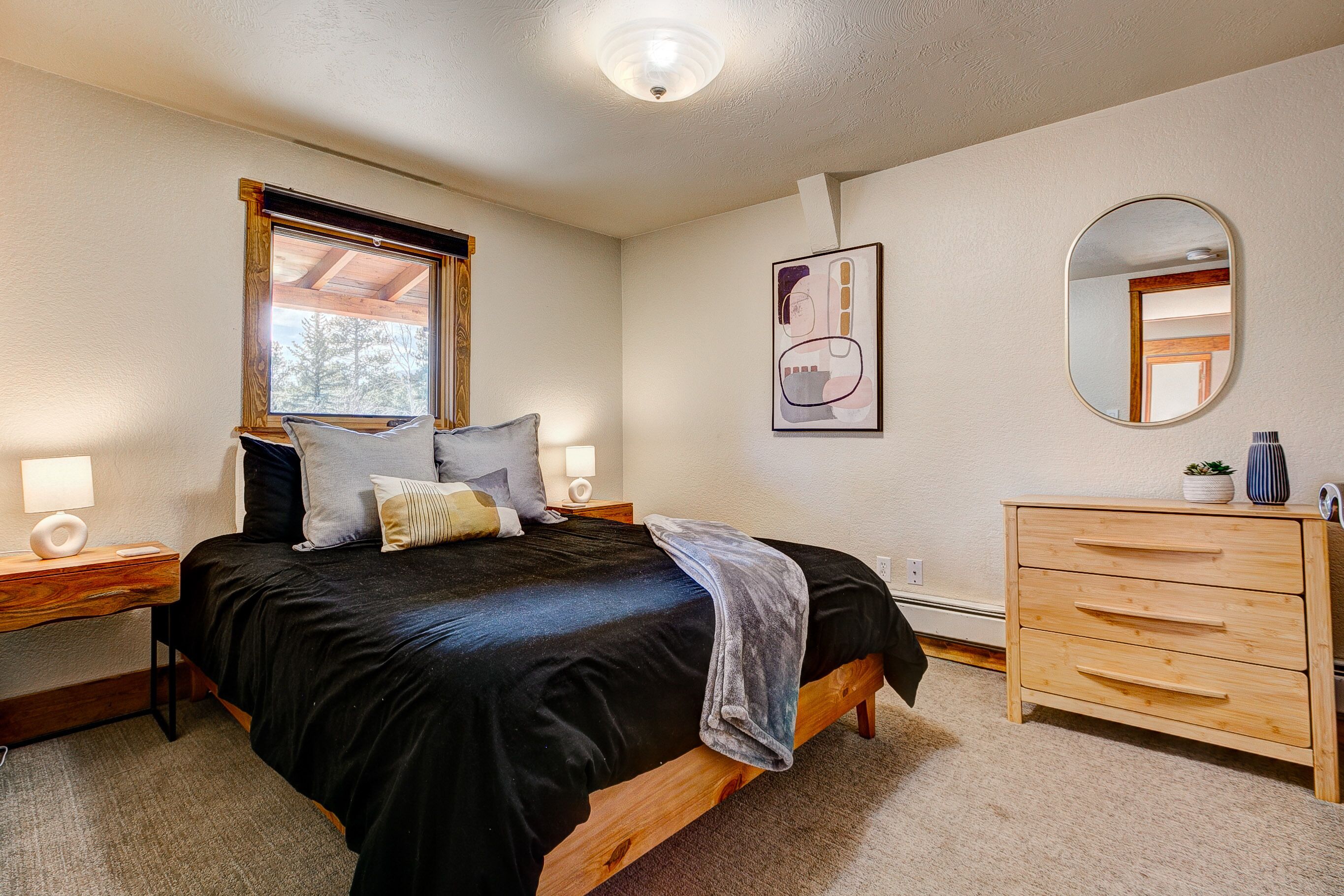 Un dormitorio con cama, mesitas de noche, cómoda, espejo y ventana.