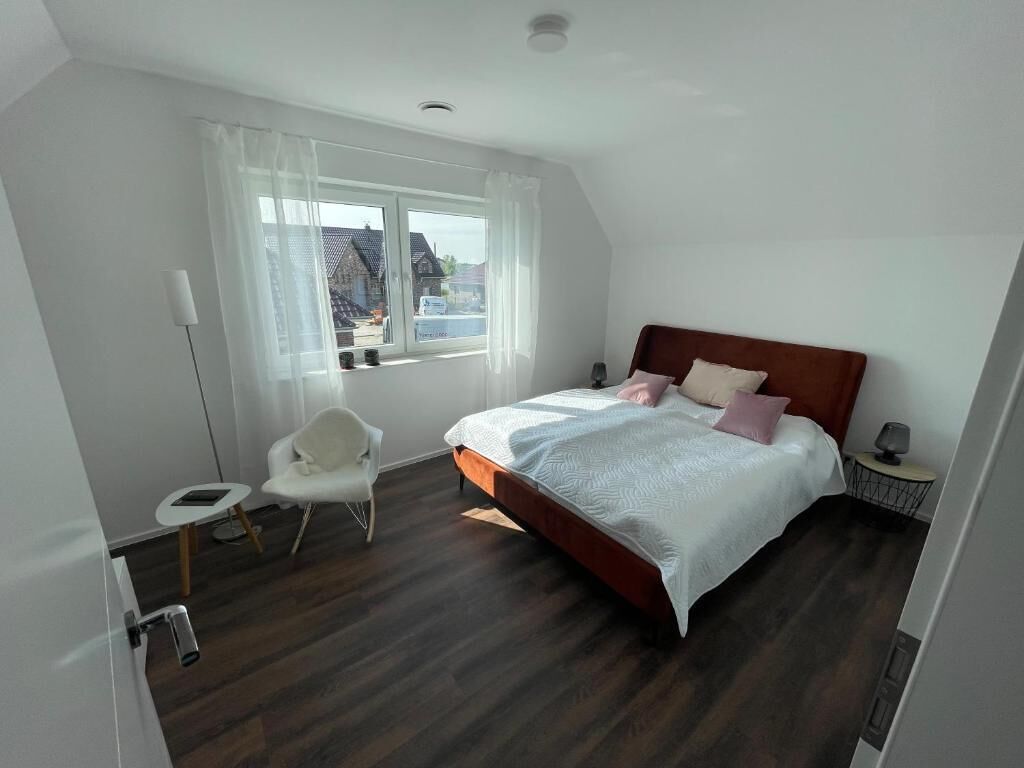A bedroom with a bed, a chair, a bedside table, and a window.