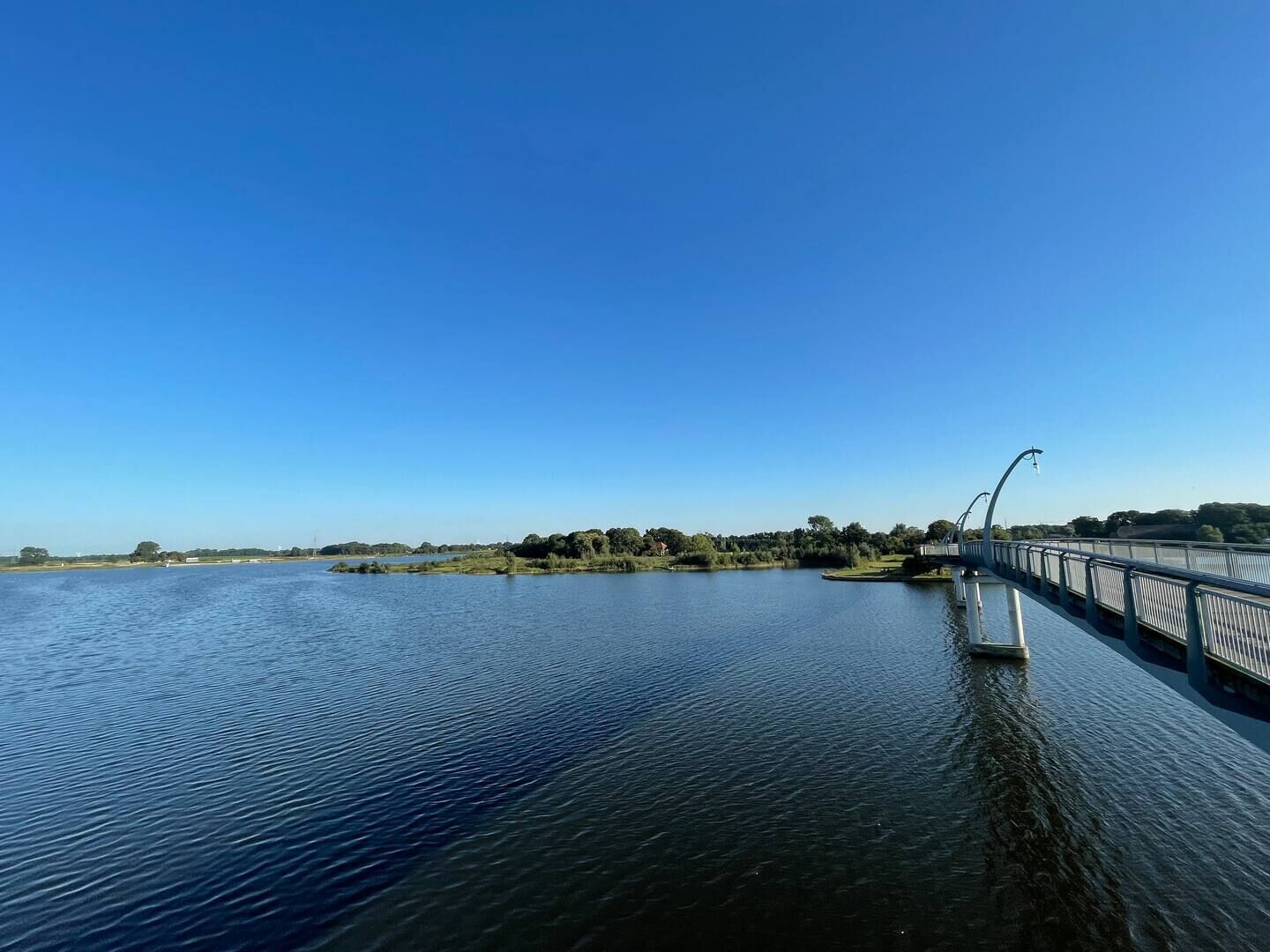 Eine Brücke über ruhigem Wasser, bewölkter, klarer Himmel.