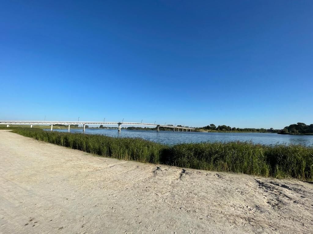 A sandy beach with a river and a bridge in the background.