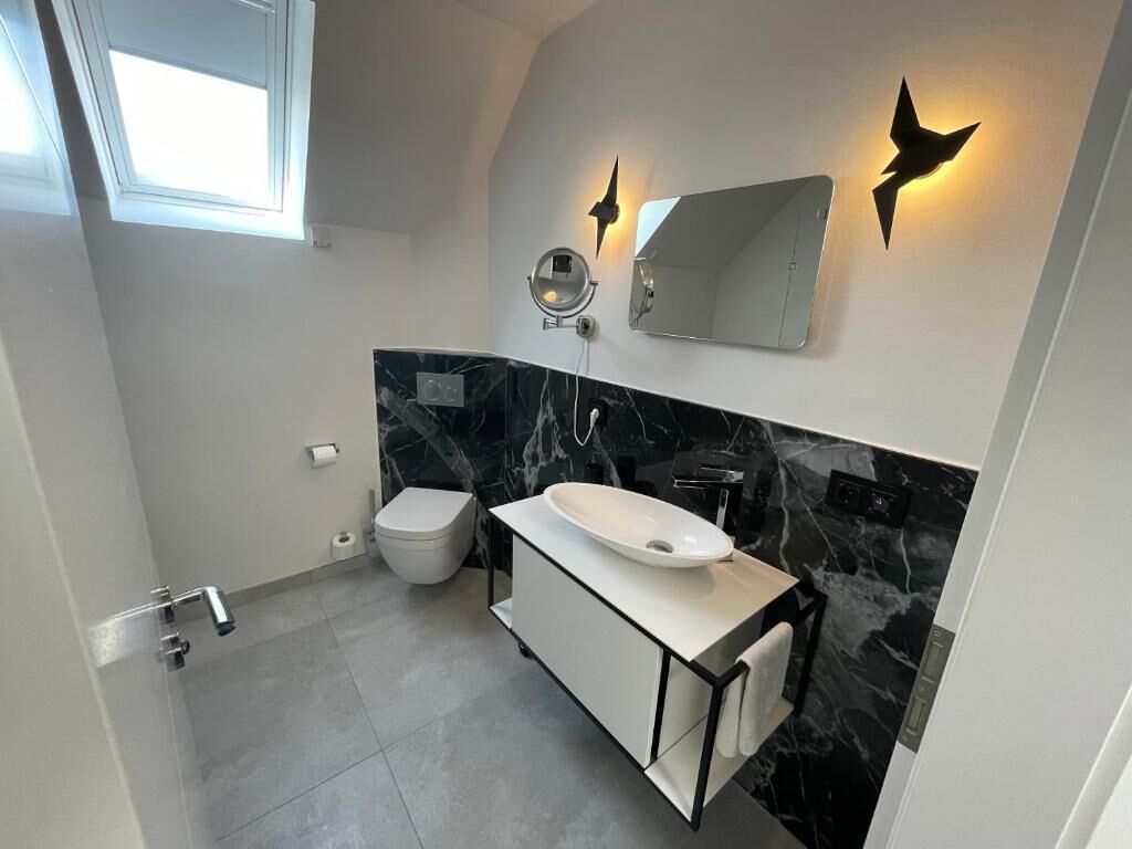A modern bathroom with a white sink, black marble backsplash, and a large mirror.
