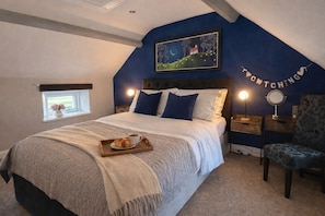 Un dormitorio con cama, una mesita de noche con lámpara, una silla, una ventana con vistas y un cuadro en la pared.