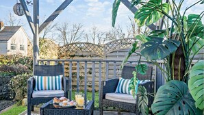 Un patio al aire libre con mobiliario de mimbre, una mesa con bebidas y plantas tropicales.