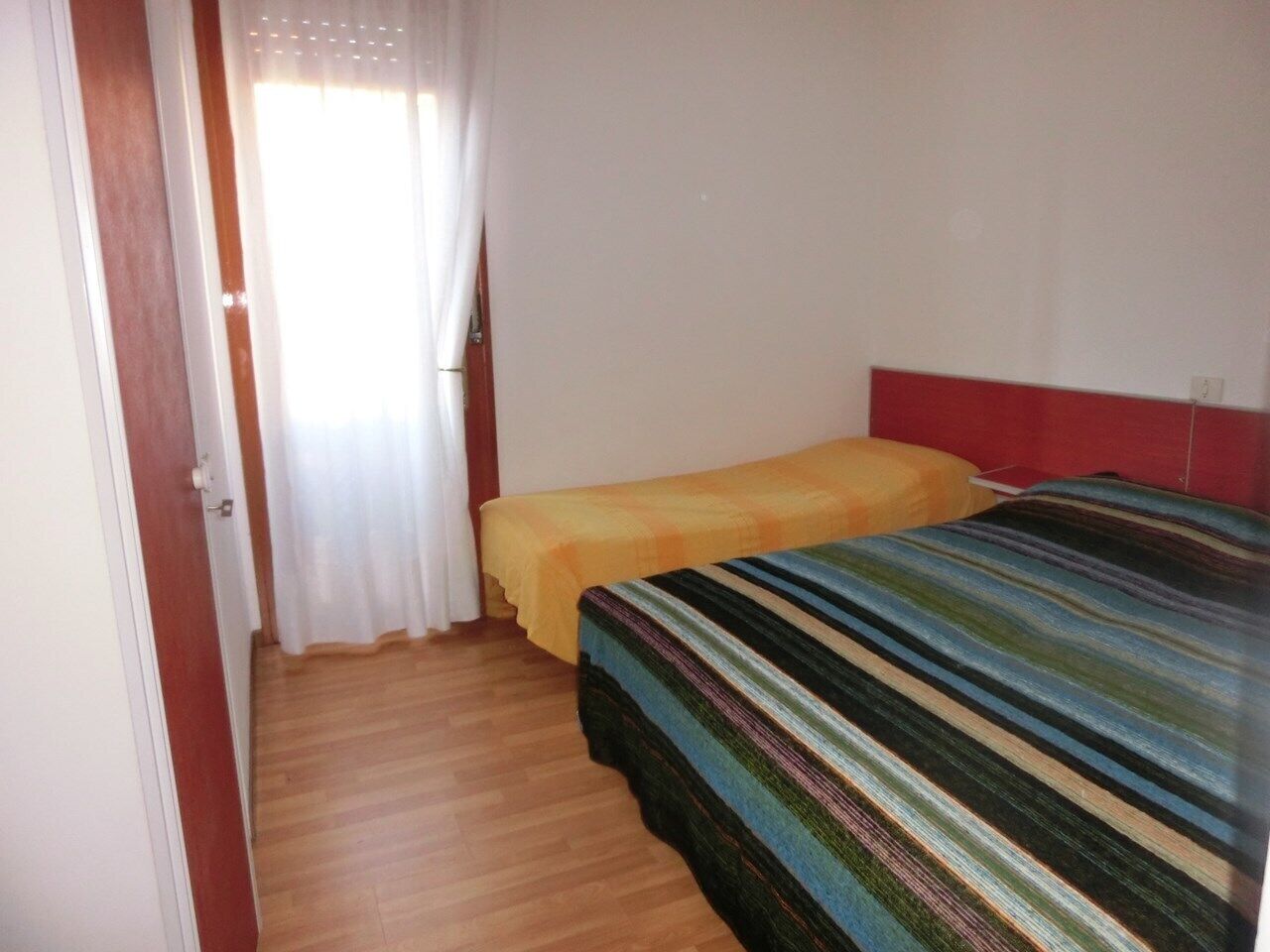 Une petite chambre avec deux lits, l’un recouvert d’une couvre-lit à rayures et l’autre d’une simple couverture jaune.