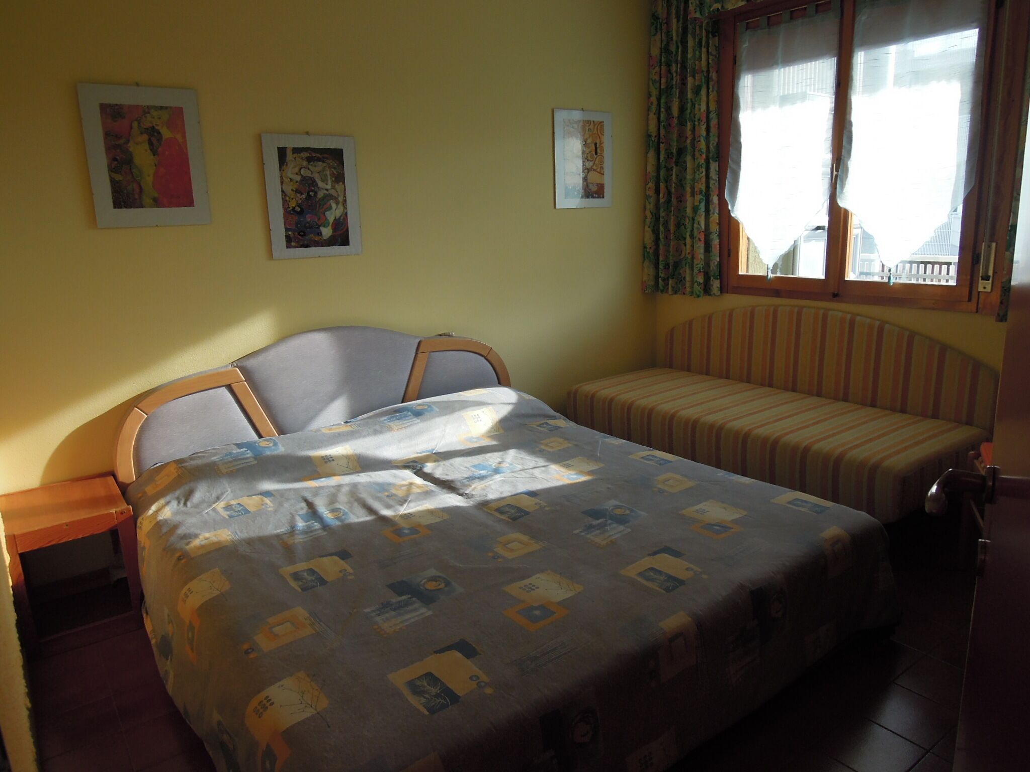 Une chambre à coucher avec un lit, un banc et trois tableaux encadrés accrochés au mur.