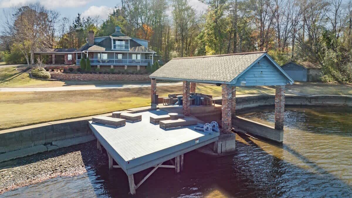 A dock with a covered seating area and a house in the background.