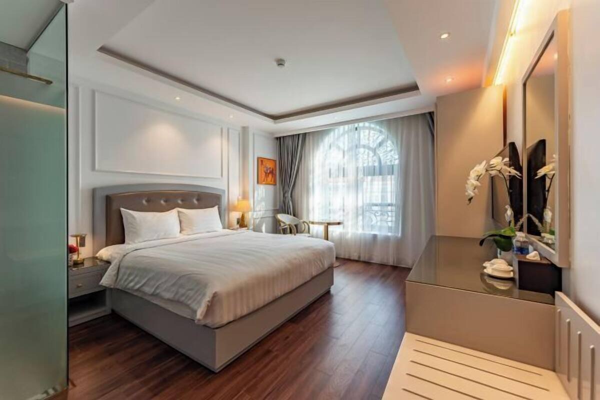 Moderni hotellihuone, jossa on suuri sänky, yöpöydät, työpöytä ja peili.