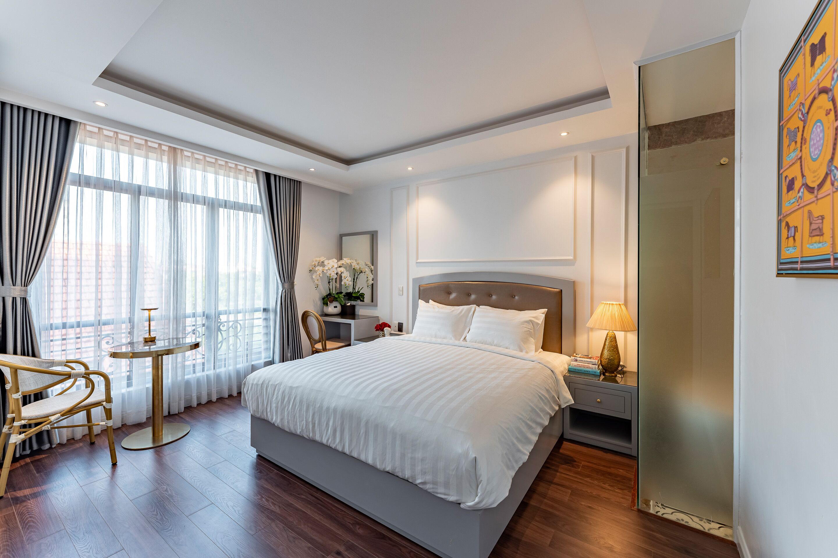 A modern hotel room with a large bed, a small round table, a chair, and a nightstand with a lamp.