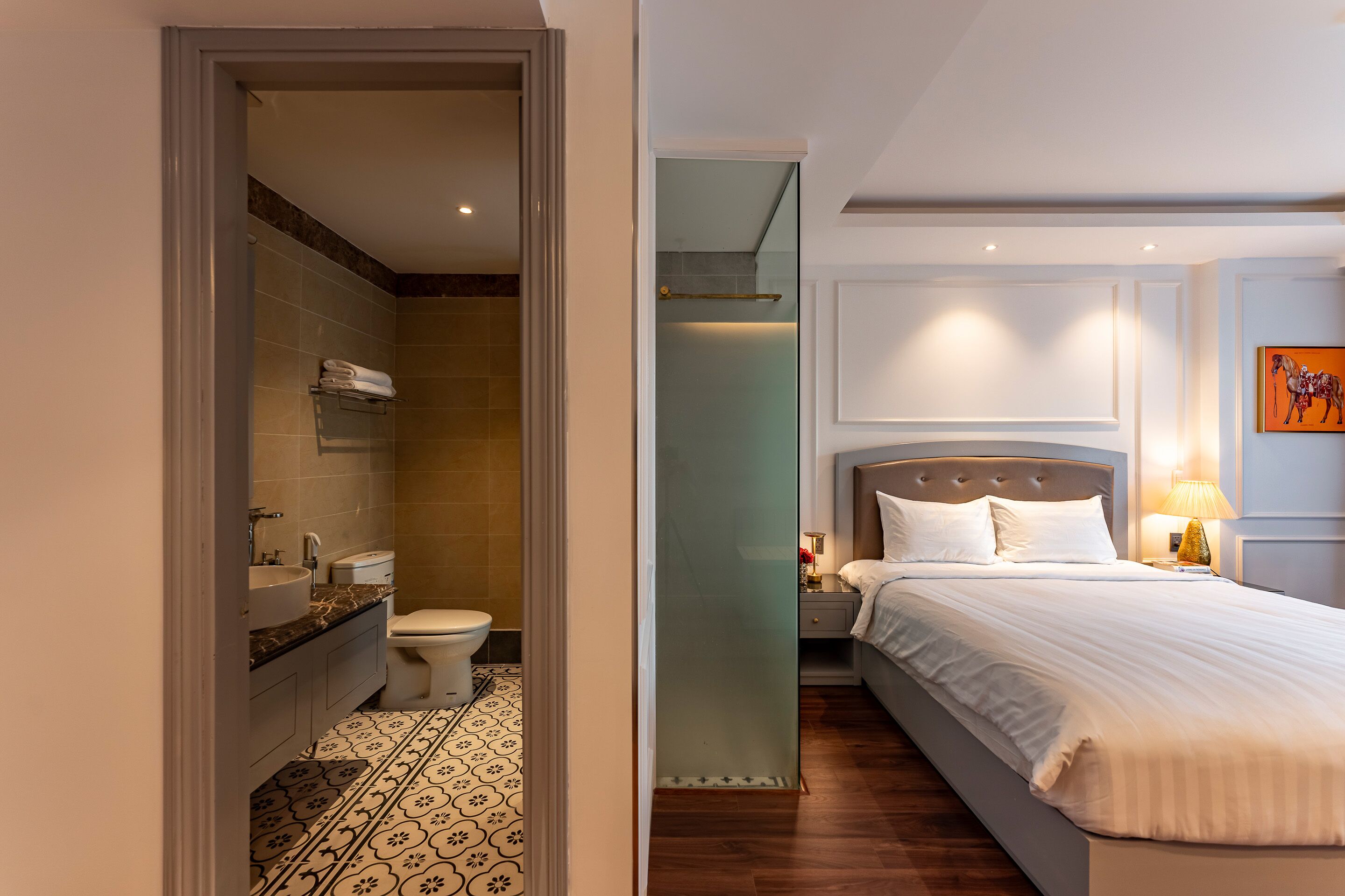 Une chambre d’hôtel avec une salle de bain, un lit, une table de chevet et un tableau au mur.