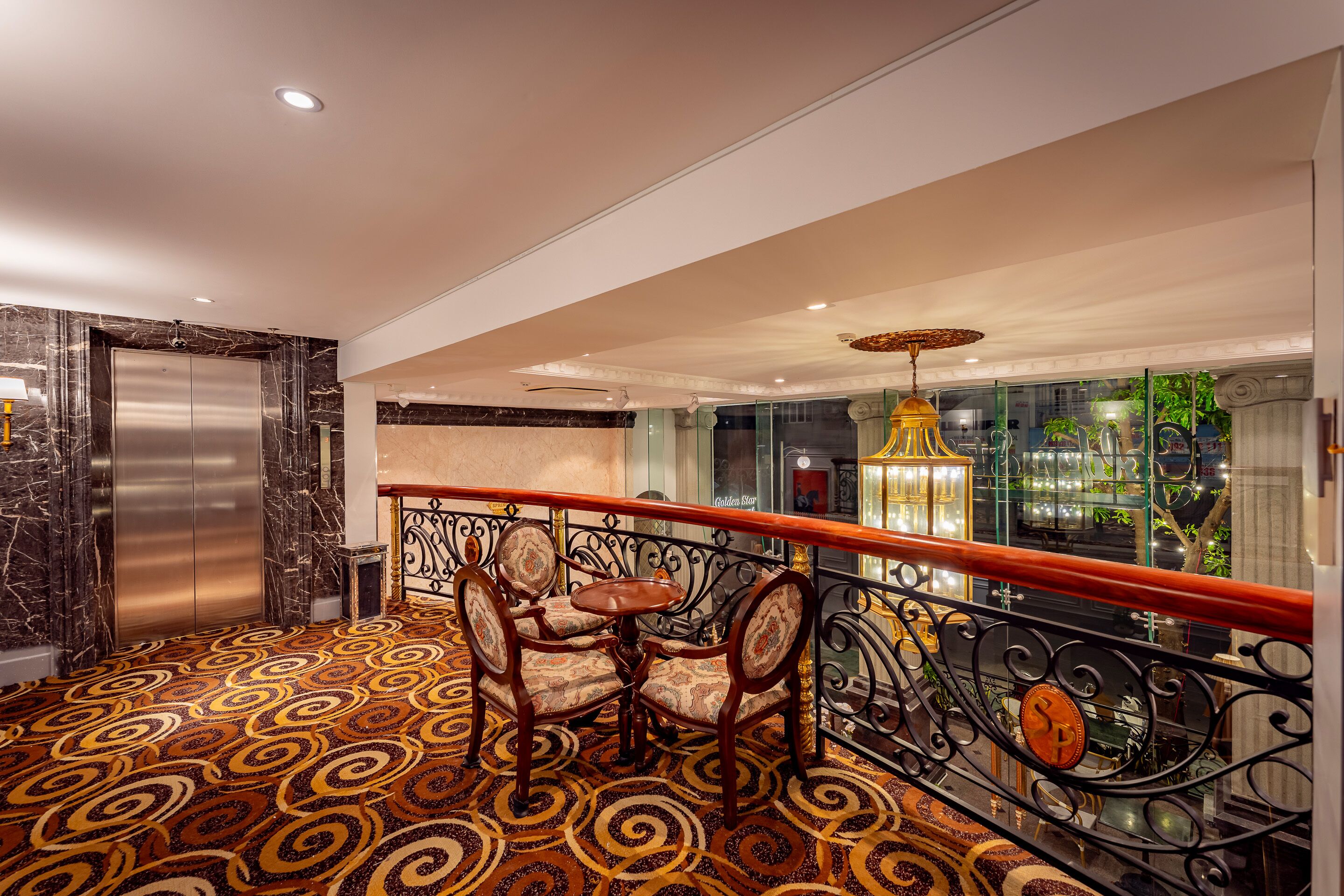 A hotel lobby with a patterned carpet, a chandelier, and a view of the outside.