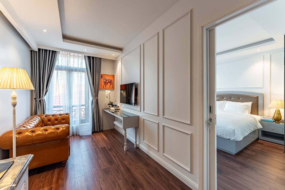 Moderni hotellihuone, jossa on nahkasohva, työpöytä, sänky ja televisio.