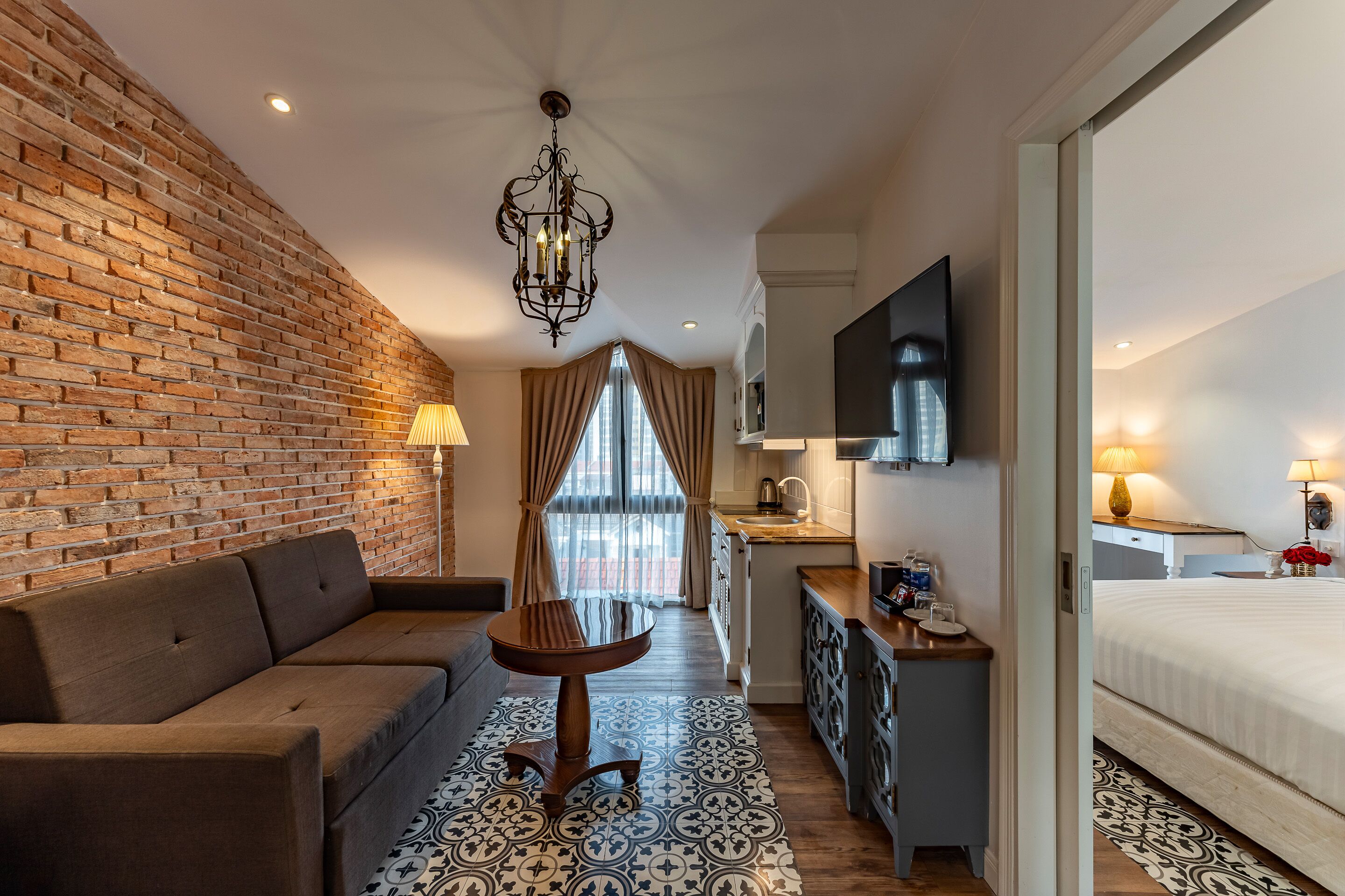 Een moderne hotelkamer met een geaccentueerde bakstenen muur, een bank, een eettafel, een keukenhoek en een groot bed.