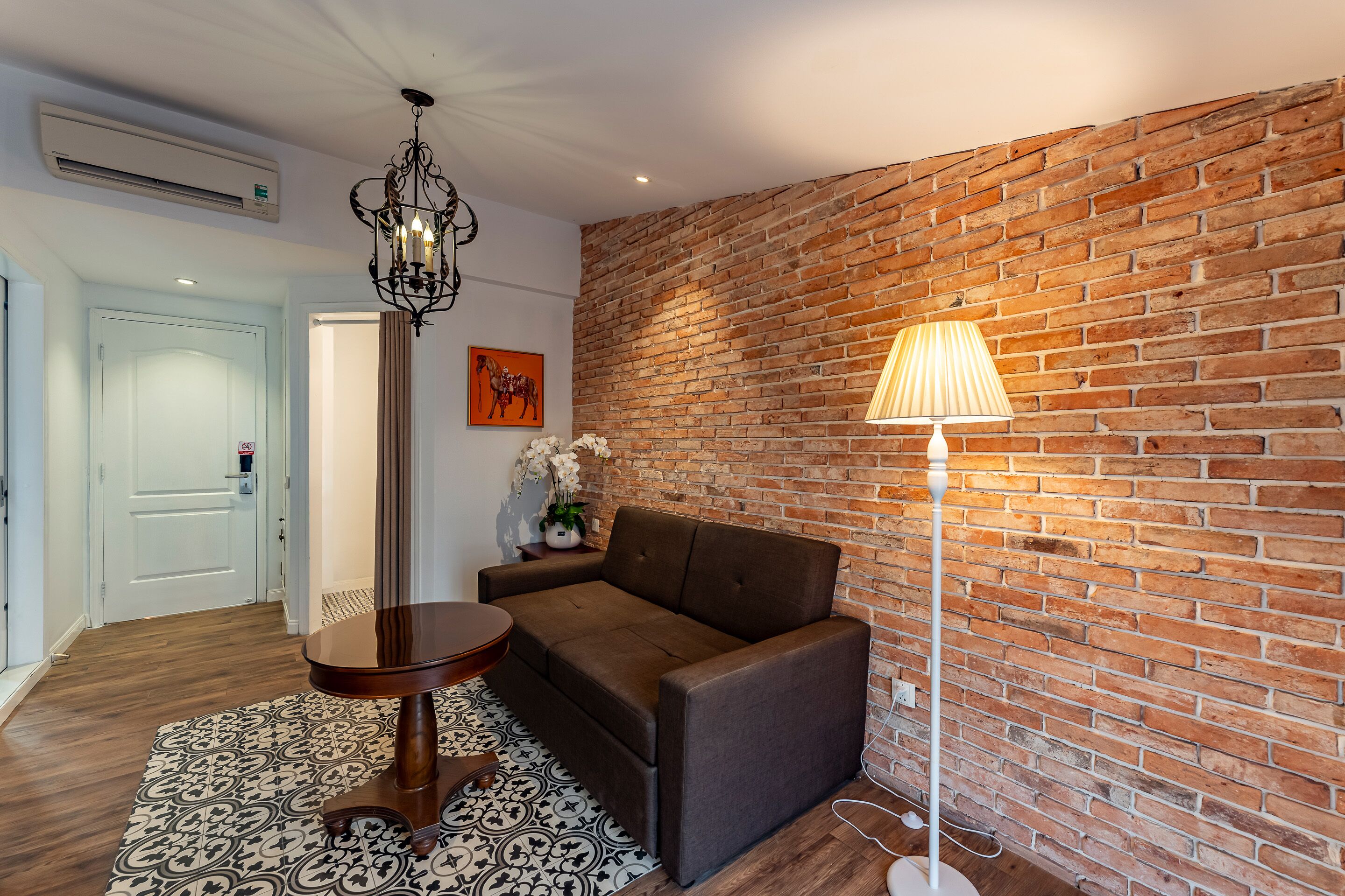 Une pièce chaleureuse avec un mur en briques, un canapé marron, une table ronde et un lampadaire.