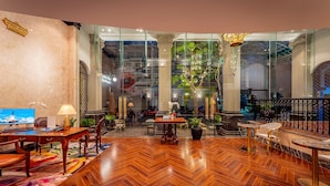 A spacious lobby with a herringbone wood floor, a reception desk, seating areas, and a large glass wall offering a view of the street.