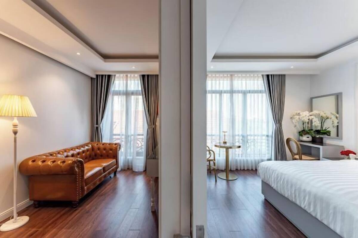 Hotellihuone, jossa on nahkasohva, pyöreä pöytä, valkoisilla tekstiileillä varustettu sänky ja suuri ikkuna, josta avautuu näkymä kaupunkiin.