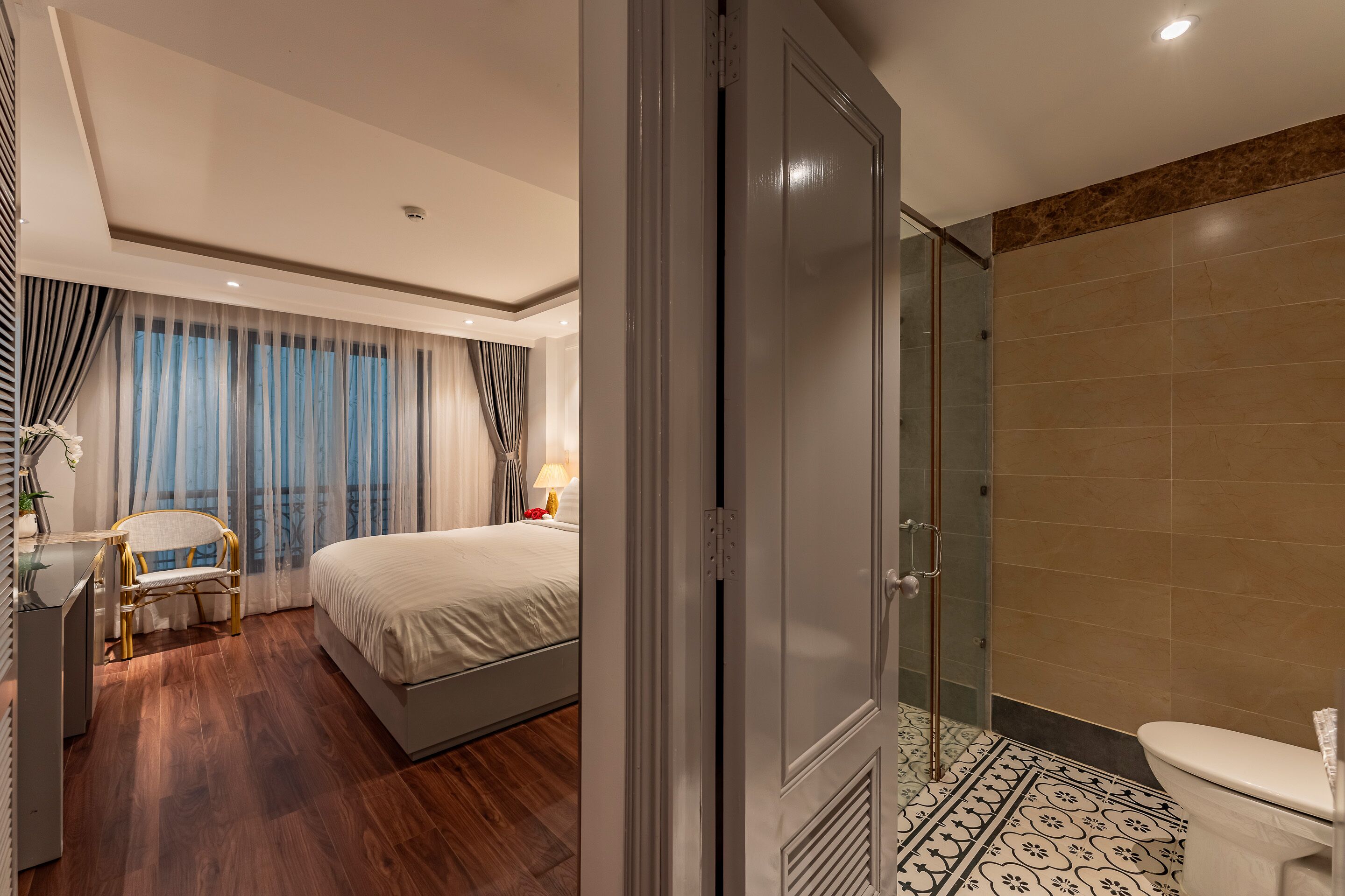 A hotel room with a bed, a chair, a desk, a shower area, and a toilet.