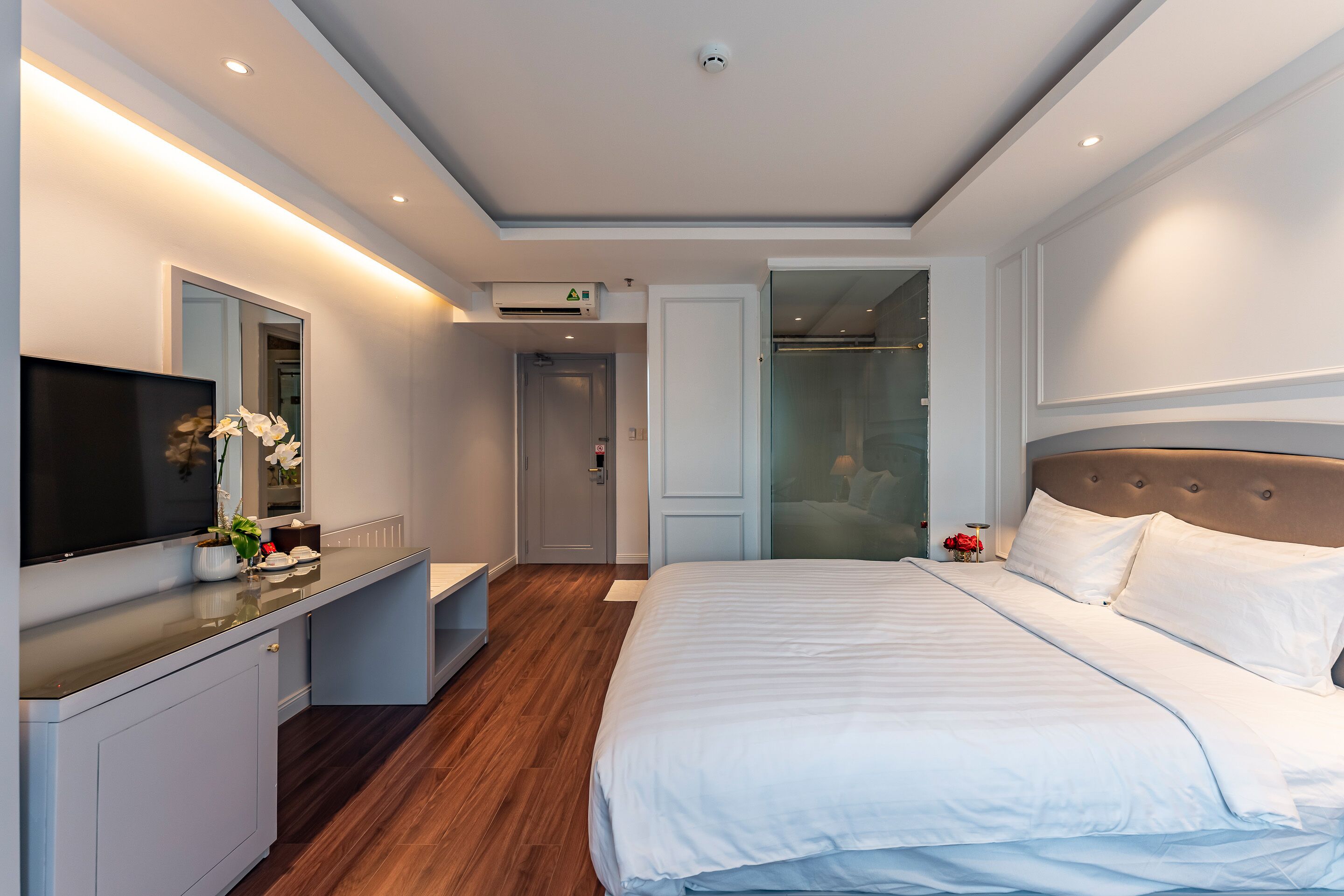 Ein modernes Hotelzimmer mit einem großen Bett, einem Flachbildfernseher, einem Schminktisch mit Spiegel und einem begehbaren Kleiderschrank.