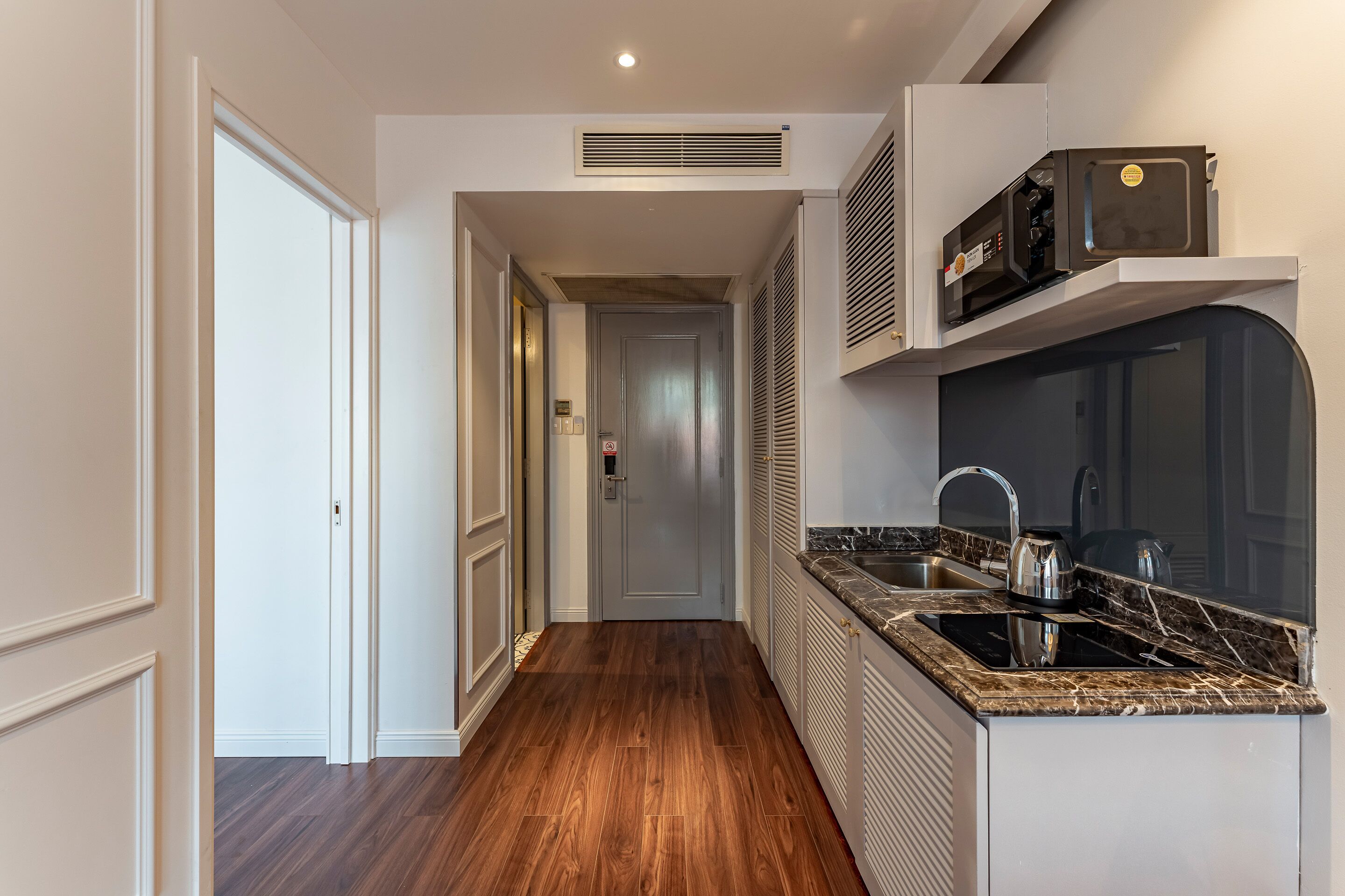 A narrow hallway with a kitchen area on the right, featuring a sink, stove, and microwave.