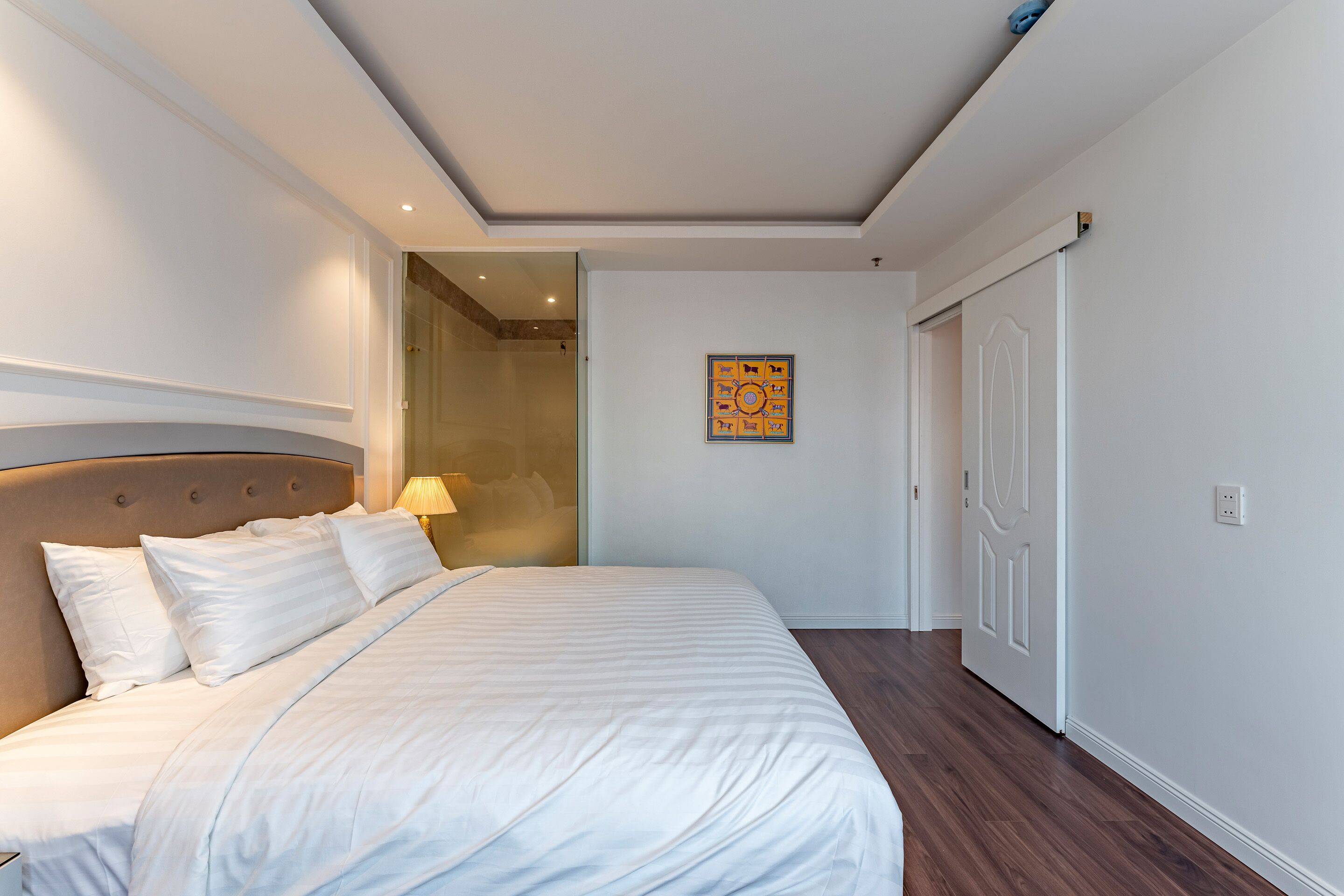 A bedroom with a large bed, a headboard, a wall-mounted artwork, and a door.