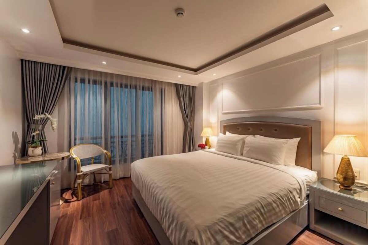 A modern hotel room with a large bed, bedside tables, a desk, and a chair.