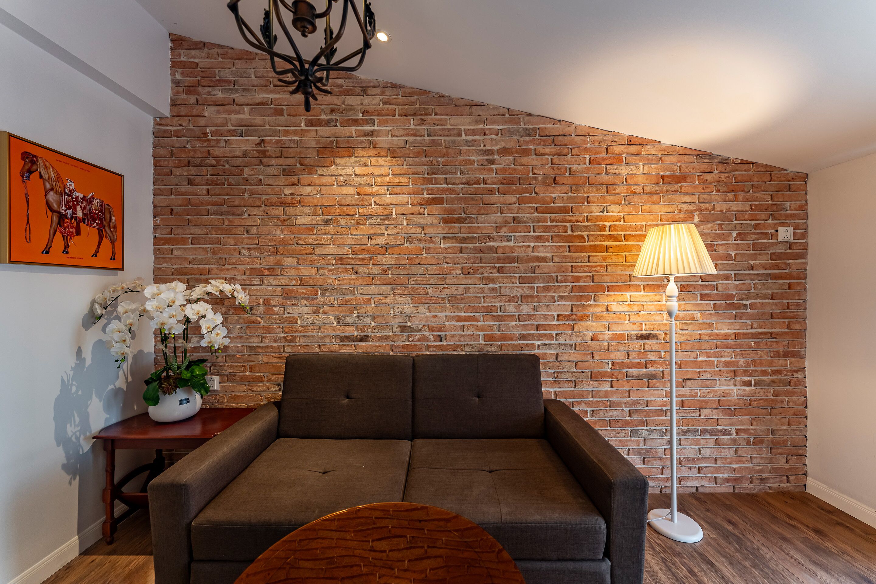 A modern living room with a brick wall, a sofa, a floor lamp, and a small table with a plant.