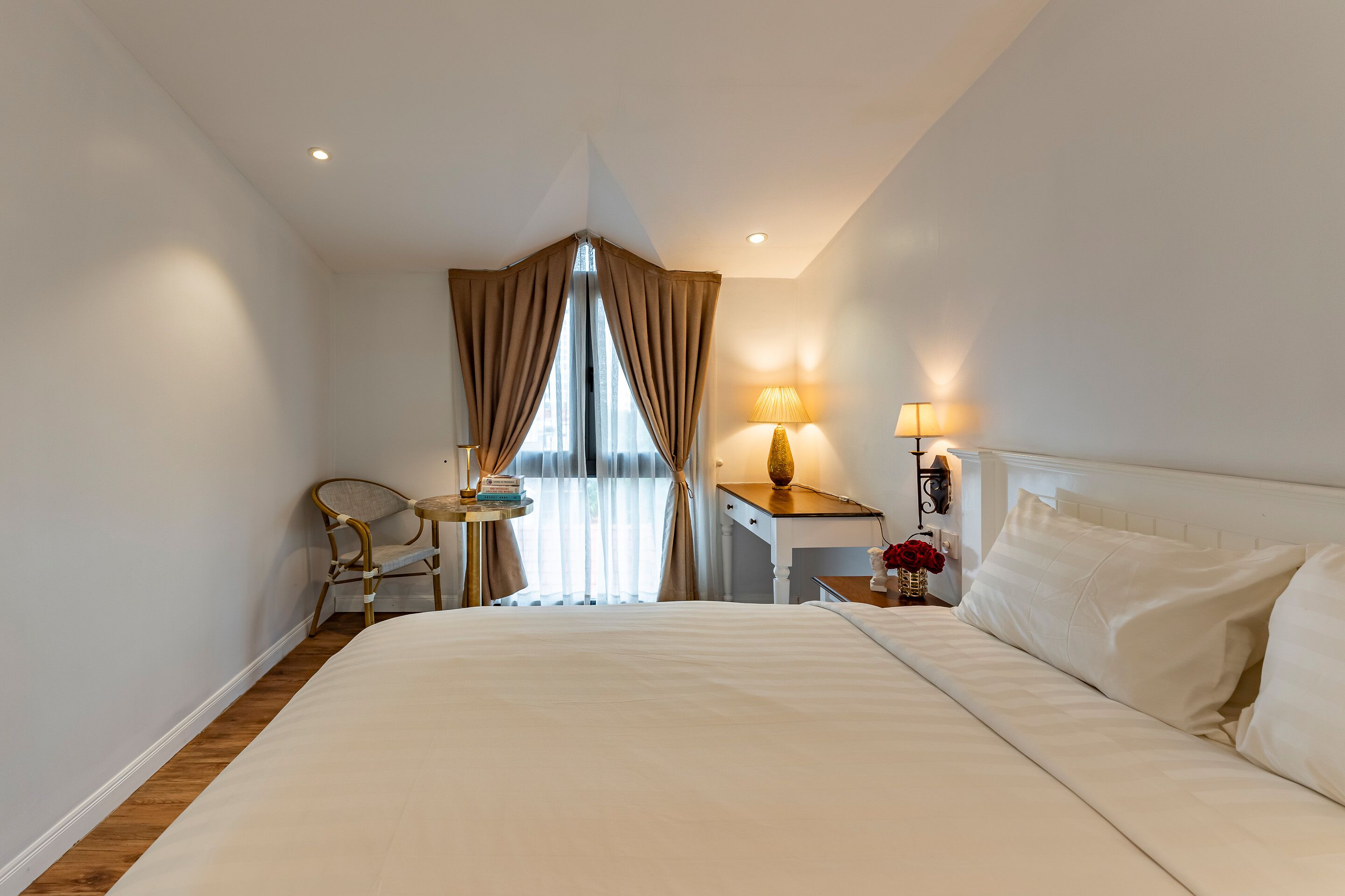 Une chambre d’hôtel avec un grand lit, un bureau avec une chaise, une lampe et une fenêtre avec des rideaux.