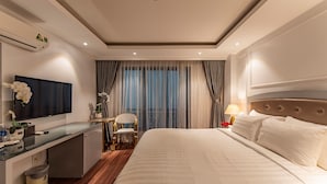 A hotel room with a bed, a desk with a TV, a chair, and a window with curtains.