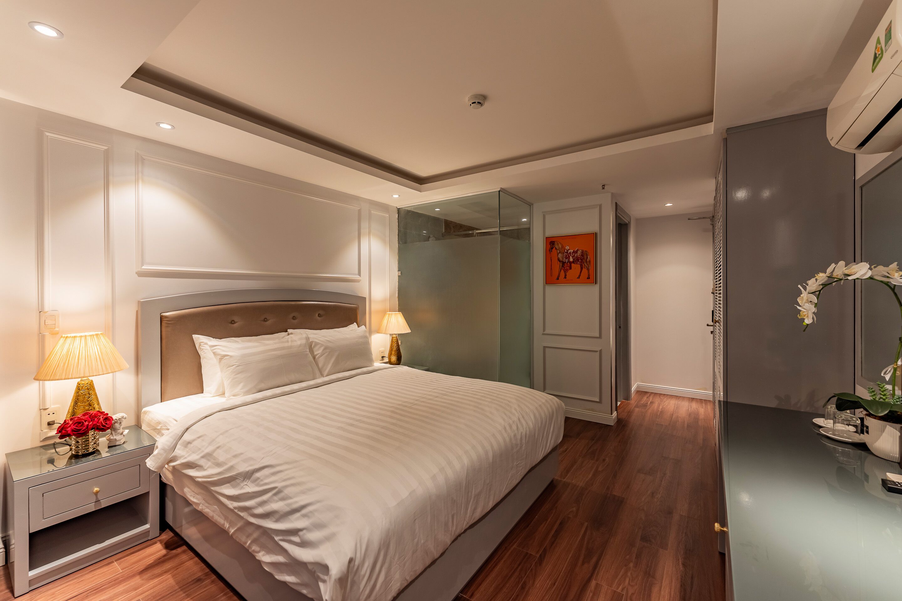 A modern bedroom with a large bed, bedside lamps, a nightstand, and a glass shower enclosure.