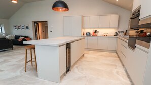 A modern kitchen with white cabinetry, a central island, and a black pendant light. - Grange Barn (Shrewsbury)