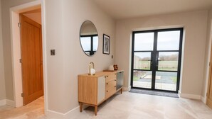 A spacious room with a wooden cabinet, a round mirror, and a large sliding glass door leading to an outdoor area. - Grange Barn (Shrewsbury)