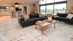 A spacious living area with two dark sofas, a coffee table with books, and a large window offering a view of the outdoors. - Grange Barn (Shrewsbury)