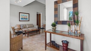 A living room with a sofa, chairs, a coffee table, a wooden console table with decorative items, and a large mirror.