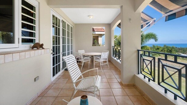 A balcony with white chairs, a table, and a view of the ocean.
