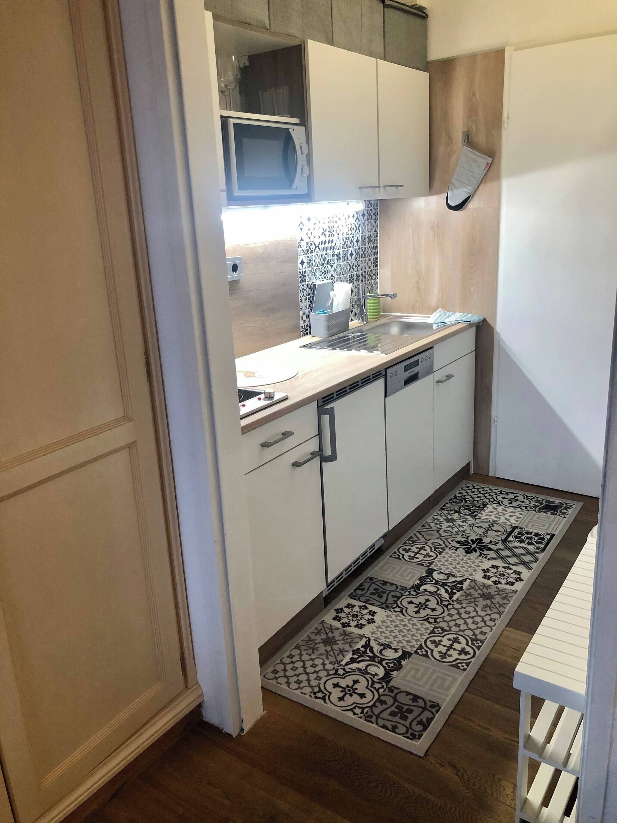A compact kitchen with white cabinets, a built-in microwave, a sink, and a patterned rug.