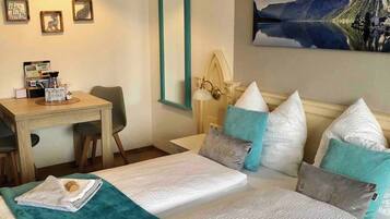 A hotel room with a bed, a desk, a chair, a lamp, and a painting of a mountain landscape.