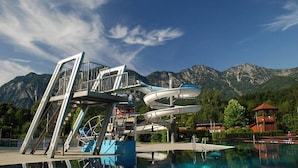 Un toboggan aquatique avec une structure métallique, une piscine et des montagnes en arrière-plan.