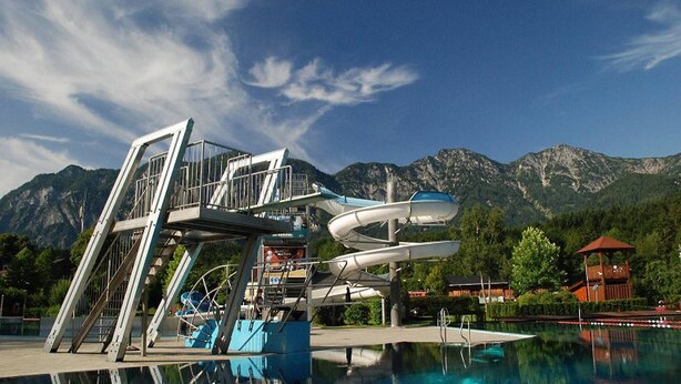 Un tobogán de agua con estructura metálica, una piscina y montañas al fondo.