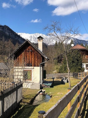 Une cabane en bois avec une cheminée, un petit étang et une montagne en arrière-plan.