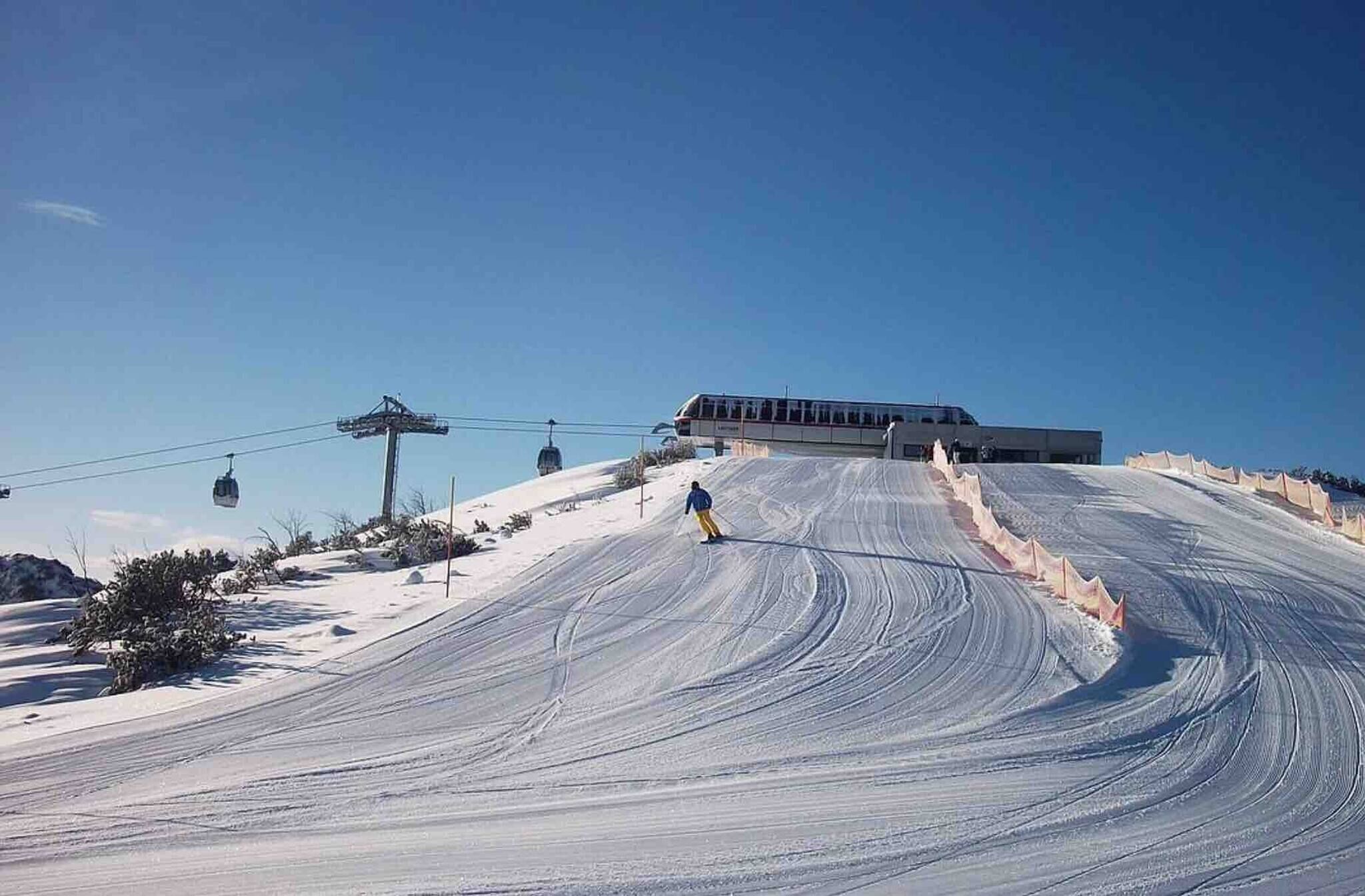 A ski slope with a cable car system and a building in the background.