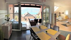 Un moderno comedor con vistas a una montaña y un lago, una puerta de cristal corredera que da a un área de estar al aire libre, y un espacio de sala de estar acogedor con un sofá y una mesa de centro.