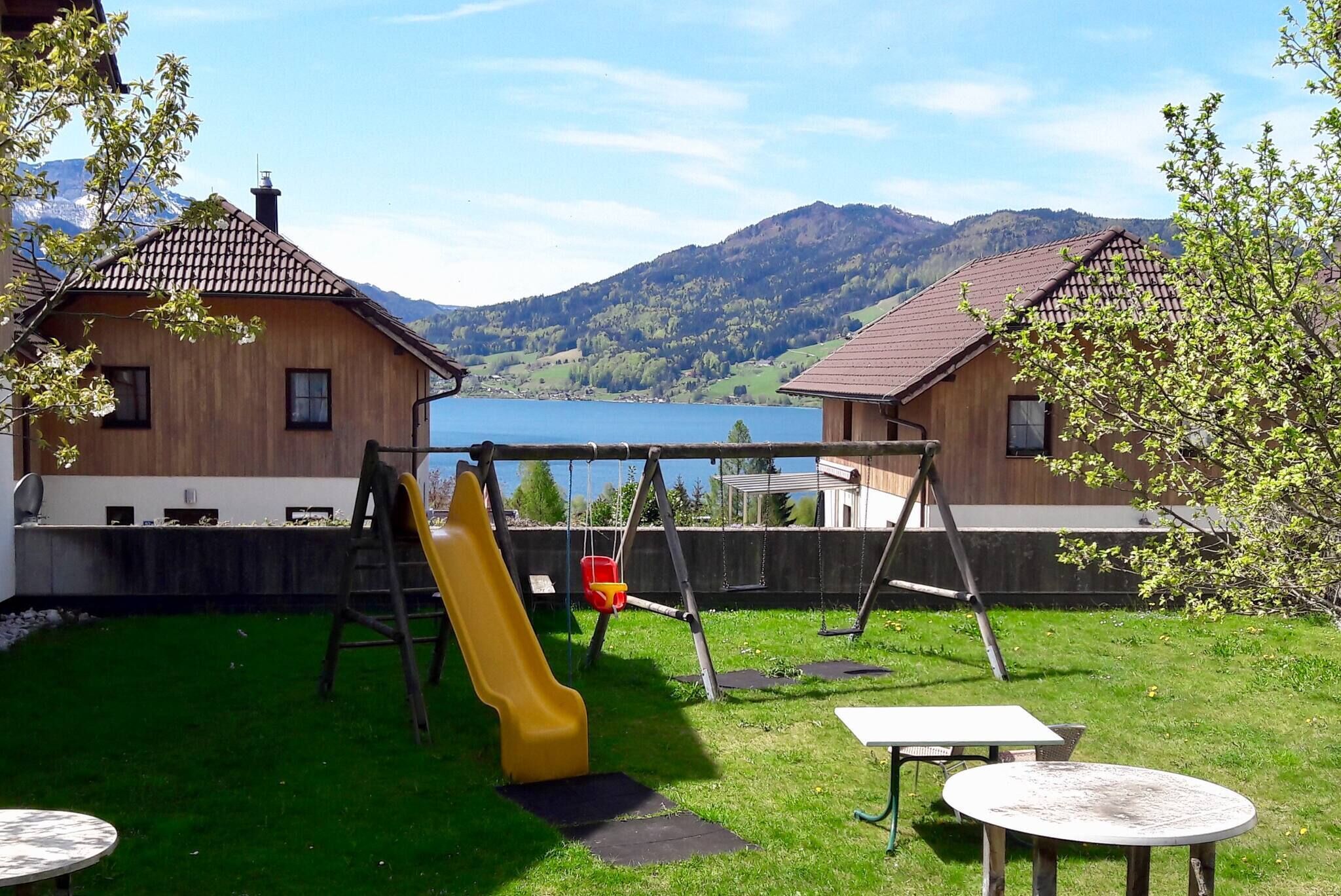Una cabaña de madera con tobogán y columpio, una mesa, y vistas a montañas y un lago.