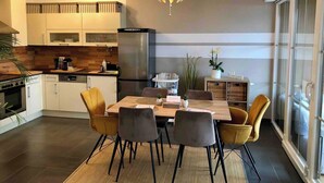 Una cocina moderna con comedor, que incluye una isla central, iluminación colgante y vistas amplias a través de grandes ventanales.