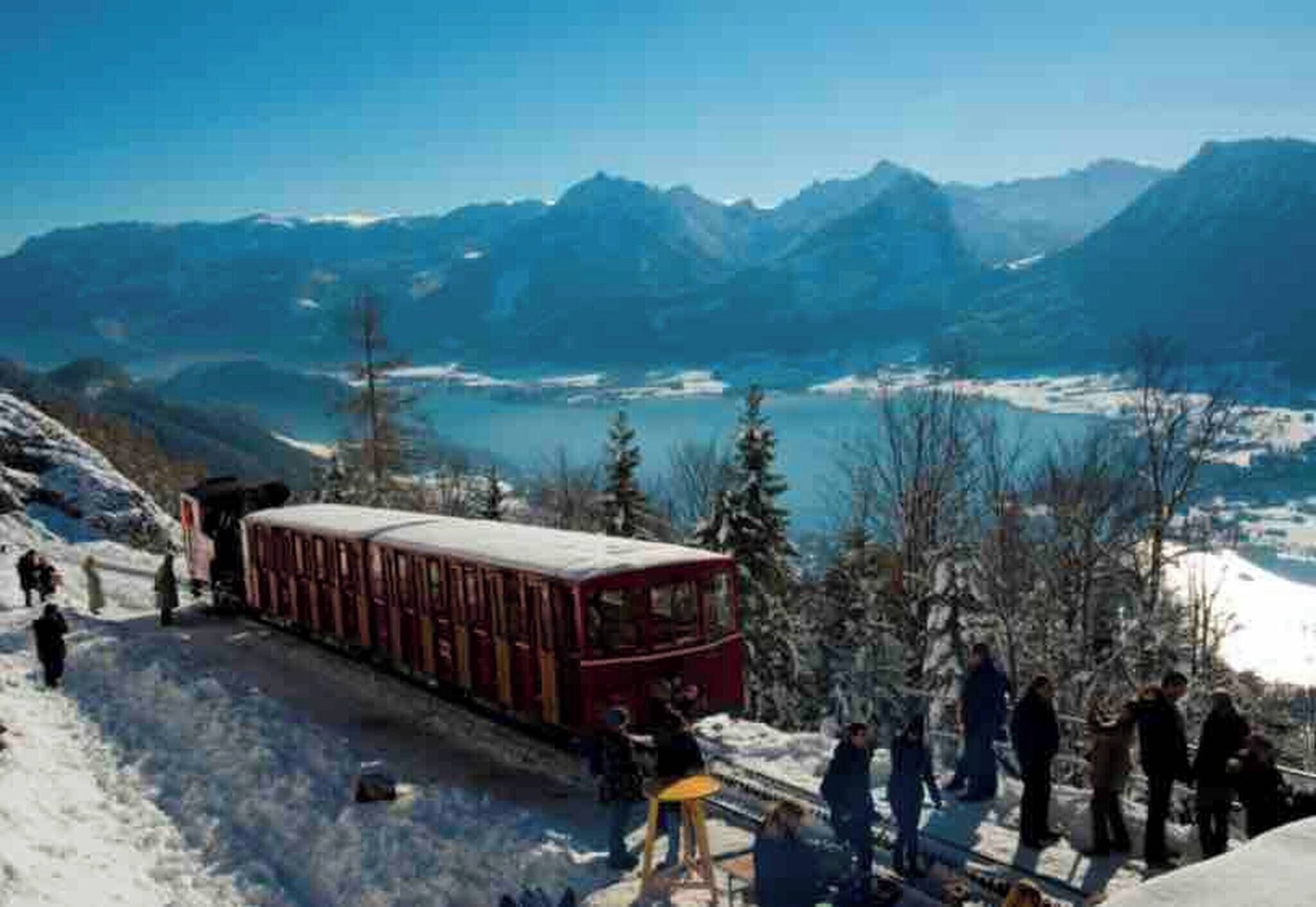 A train on a snowy mountain track with passengers, surrounded by a mountainous landscape.