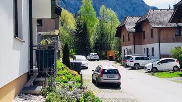 A residential street with parked cars, a building with a balcony, and a mountain in the background.