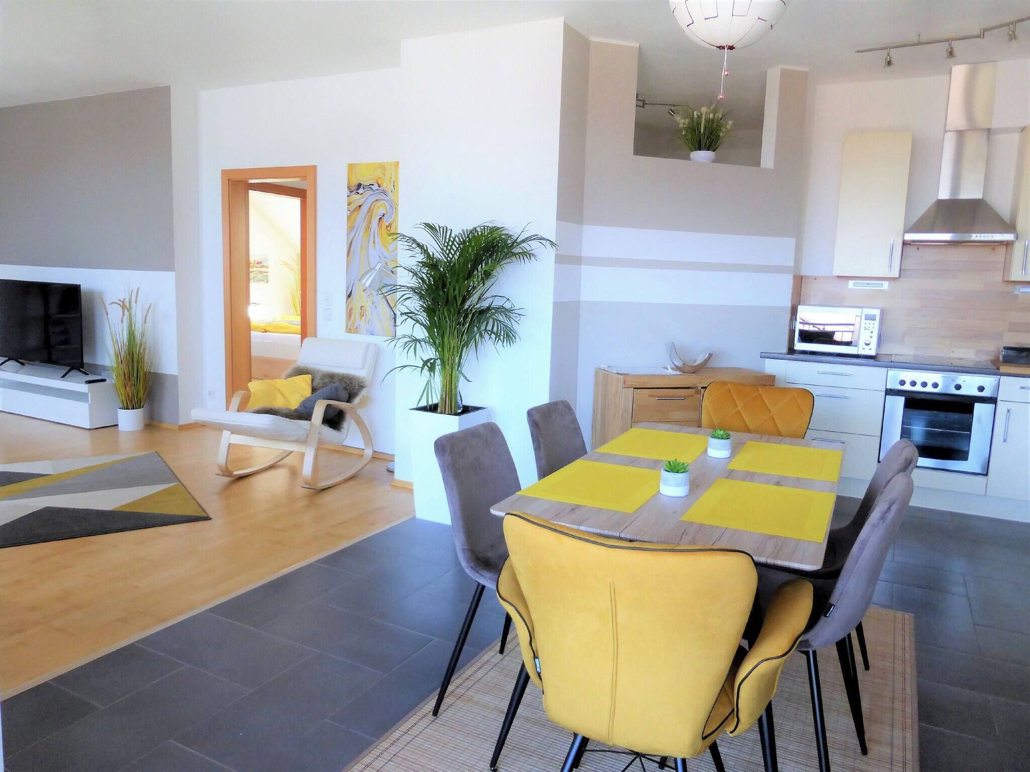 Una sala de estar moderna con un televisor de pantalla plana, un sofá, una mesa de comedor con individuales amarillos y una cocina con microondas y horno.