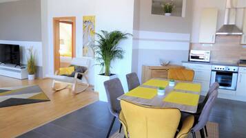 Una sala de estar moderna con un televisor de pantalla plana, un sofá, una mesa de comedor con individuales amarillos y una cocina con microondas y horno.