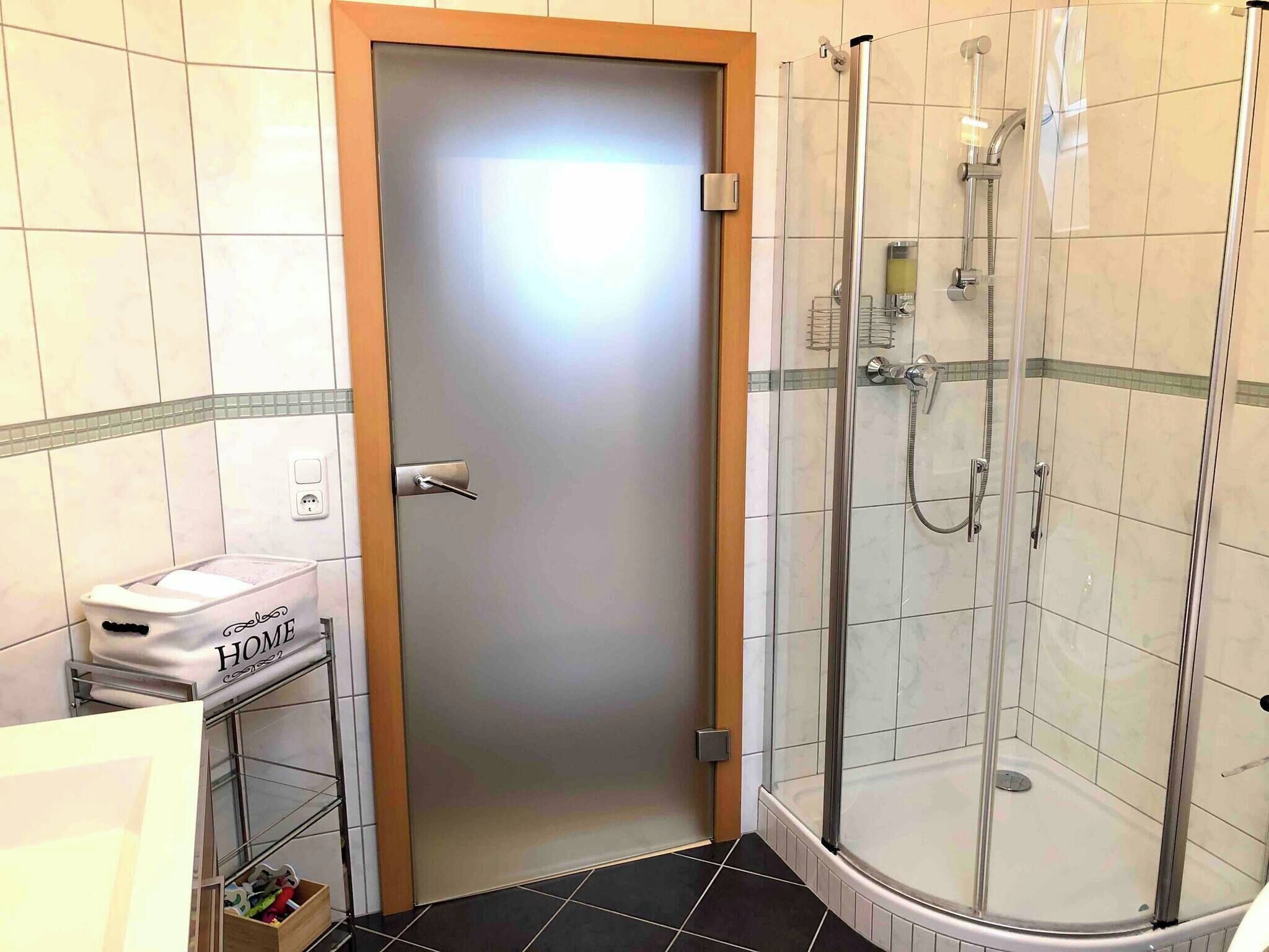 A bathroom with a glass-enclosed shower, a sink with a towel, and a door with a frosted glass panel.
